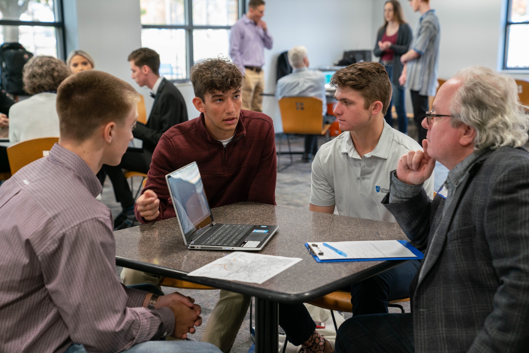 Business students discuss ideas around a table with a community business leader.